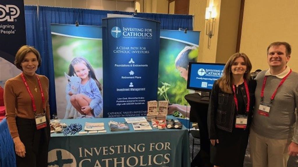 Mary Brunson, Elizabeth and John standing behind the Investing for Catholics booth, with brochures and booklets displayed on the table (photo 1 of 2)